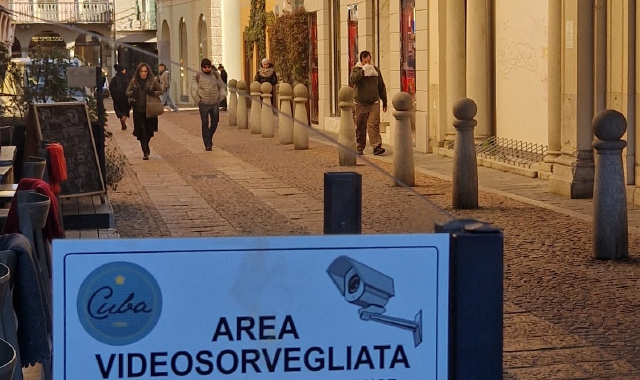 Il cartello che avvisa della presenza delle telecamere in via Del Cairo e sotto piazza del Podestà con la vetrina di Base Blu ancora “ferita” dall’auto ariete